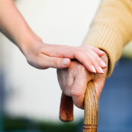 Doctor holding a senior patiens 's hand on a walking stick - special medical care concept for Alzheimer 's syndrome.